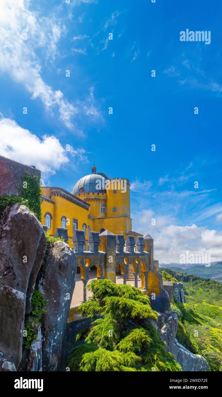 Vista esterna del cortile ad arco del Palácio da pena, dipinto di giallo, arroccato su grandi rocce con la catena montuosa di Sintra sullo sfondo unde Foto Stock