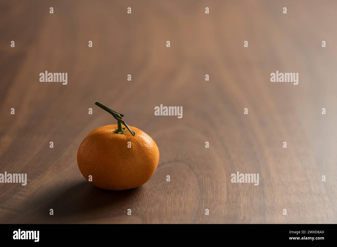 Piccolo mandarino organico con stelo su tavola in legno, messa a fuoco superficiale Foto Stock