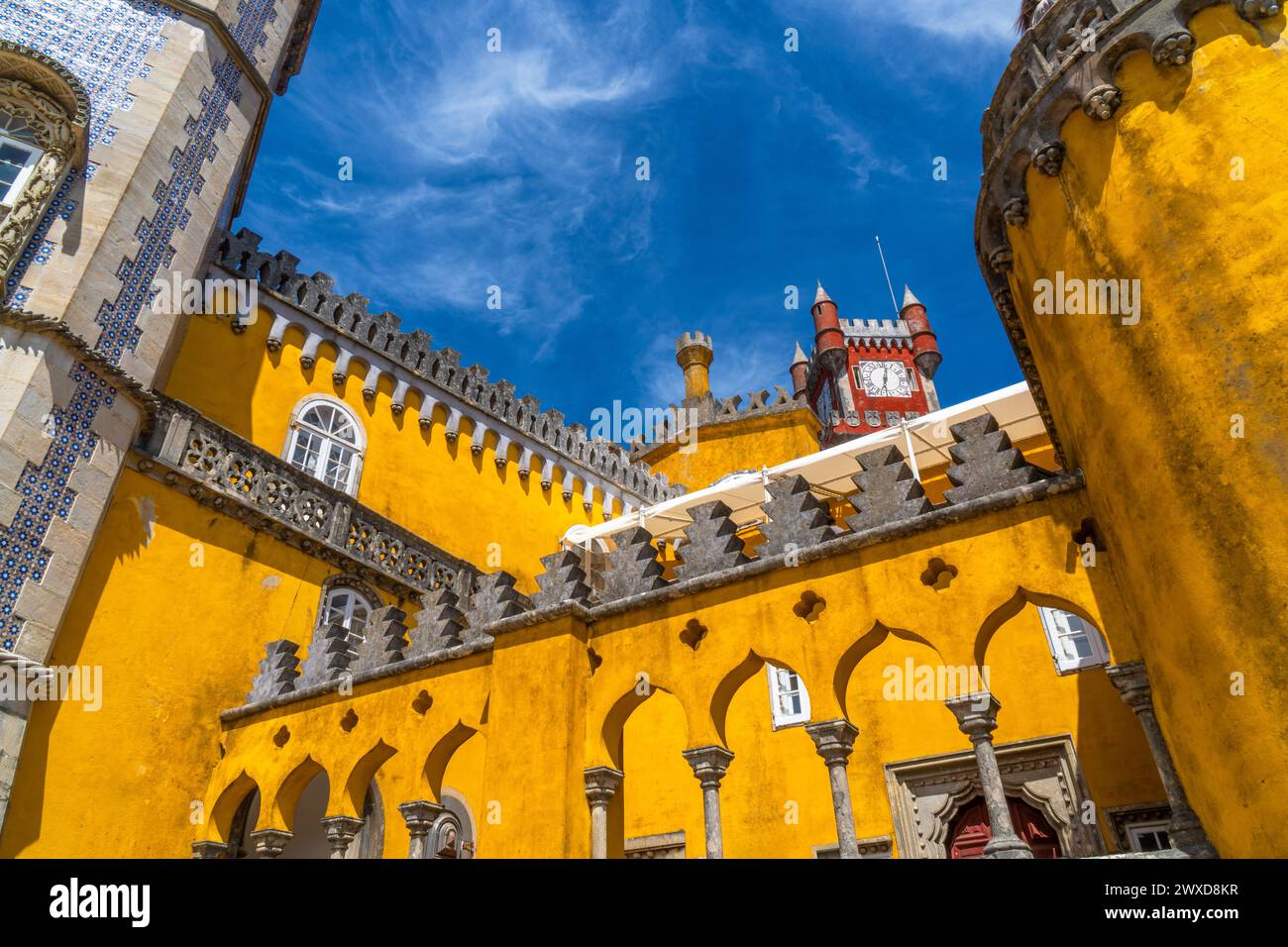 Vista ad angolo basso degli archi arabi del Palácio da pena dipinta di giallo con la torre rossa cremisi con il suo orologio in cima. A Sintra sotto un cielo azzurro e soleggiato Foto Stock