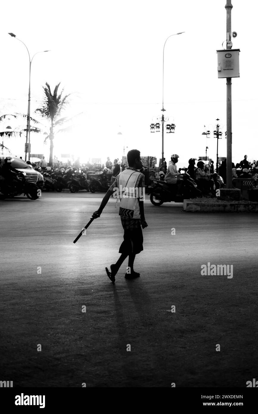 Un addetto al parcheggio indonesiano in una strada trafficata della città utilizzando un dispositivo portatile. Foto Stock
