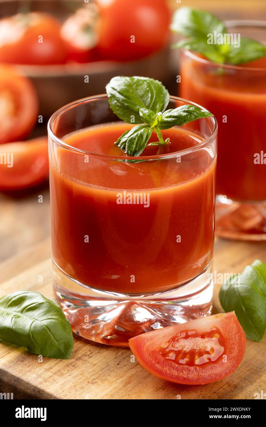Due bicchieri di succo di pomodoro con foglie di basilico e affettare i pomodori su un tavolo di legno Foto Stock