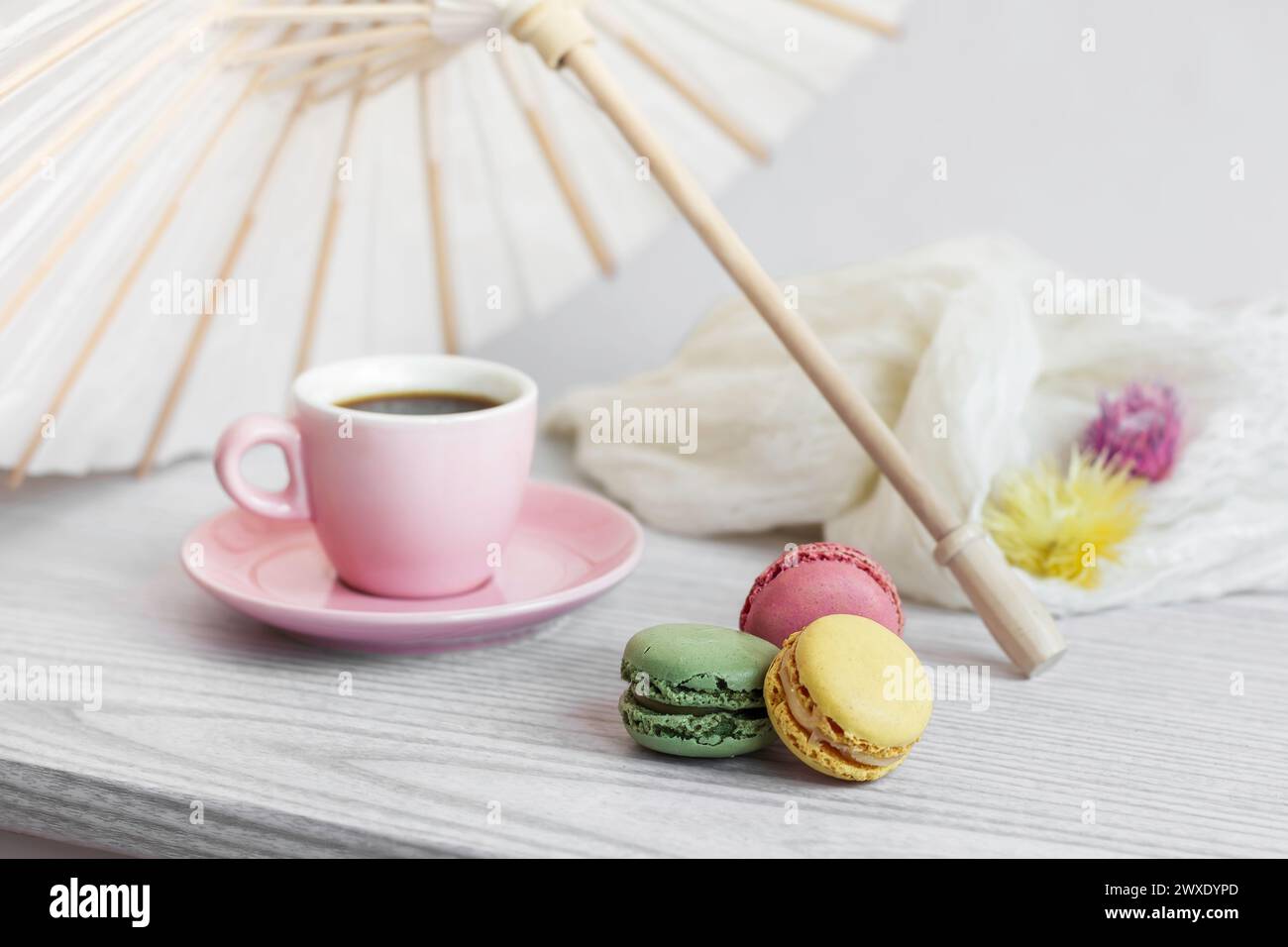 Tazza da caffè rosa e macaron colorati sotto un ombrellone di carta bianca Foto Stock Tazza da caffè rosa e macaron colorati sotto un ombrellone di carta bianca Foto Stock