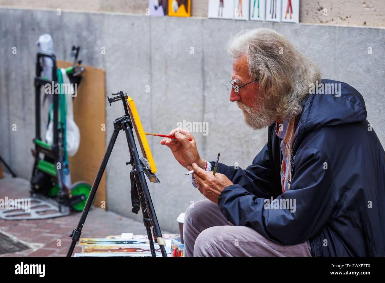 Palma di Maiorca, Spagna - 29 aprile 2023: Artista di strada che dipinge su una tela su una strada della città. L'uomo anziano si sta divertendo con uno stile di vita artistico freelance Foto Stock