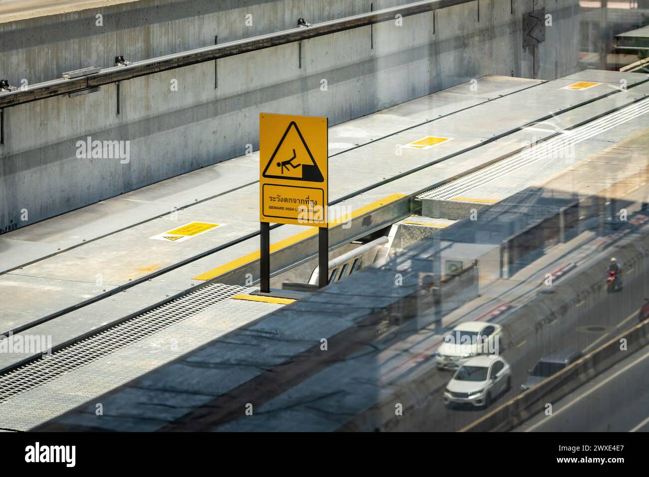 Un cartello di avvertimento su 'attenzione, caduta ad alto livello' e' visto sul terreno dove passa la monorotaia, con il riflesso della strada e delle auto sottostanti, a Bangkok. La monorotaia prodotta dalla multinazionale francese Alstom, di proprietà della Metropolitan Rapid Transit Authority (MRTA) in Thailandia, ha ripreso i servizi della linea gialla dopo che alcune parti sono cadute dall'IT, danneggiando i veicoli ma non causando lesioni. L'incidente è avvenuto due mesi fa, quando una ruota di gomma di un treno della linea gialla è caduta e ha colpito un taxi sulla strada sottostante. Foto Stock