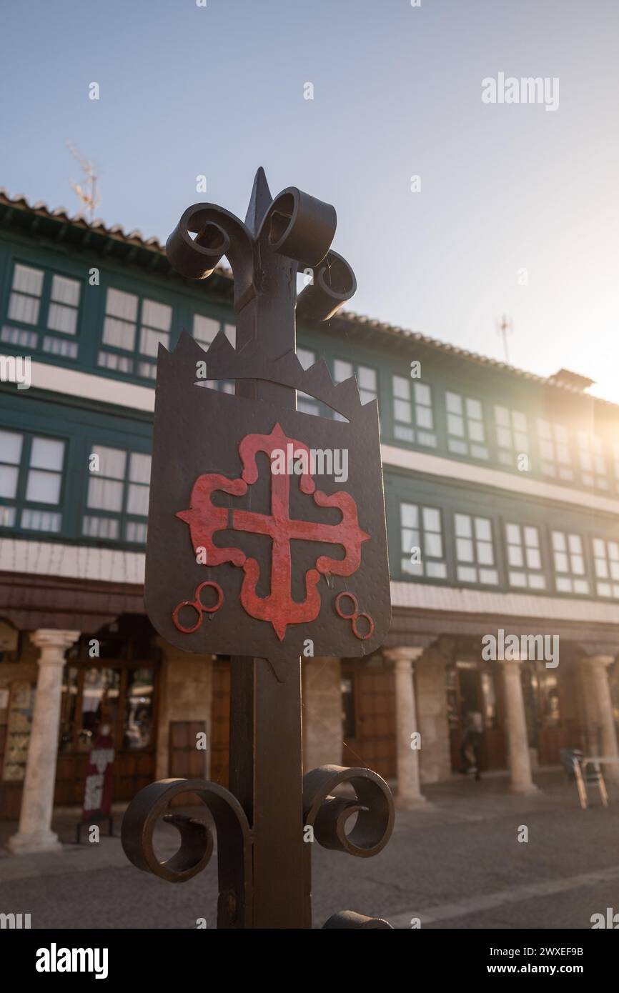 Ferro fatto emblema dell'ordine di Calatrava iluminato dal sole del mattino. Croce greca rossa con Fleur-de-lis alle sue estremità, in Plaza Mayor di Almagro Foto Stock