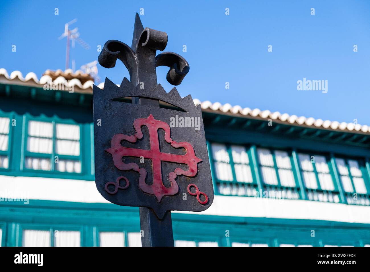 Emblema dell'ordine di Calatrava, croce greca rossa con fleur-de-lis alle sue estremità, in Plaza Mayor di Almagro, Ciudad Real con gli edifici tipici Foto Stock