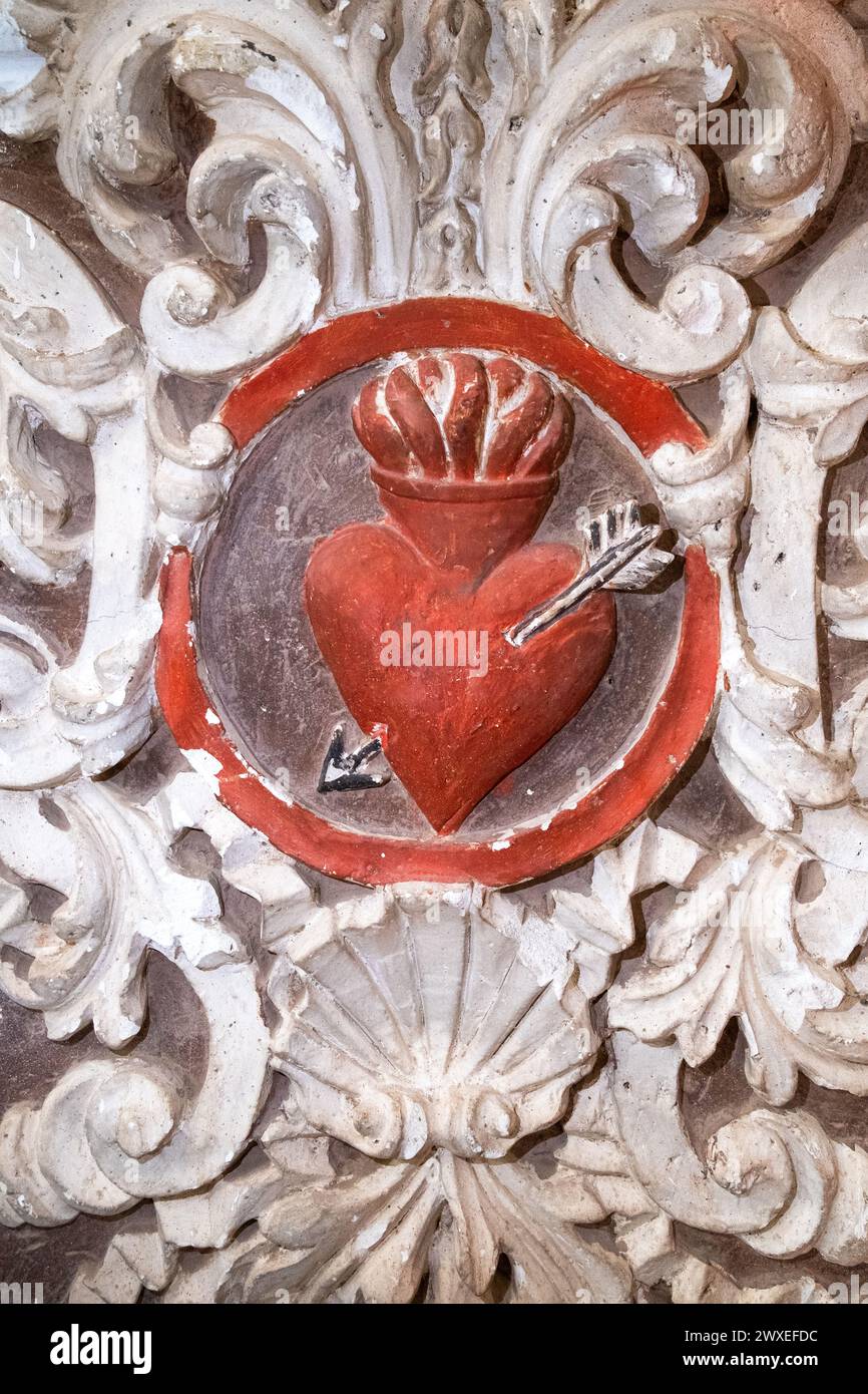 Rilievo barocco di un cuore rosso sacro trafitto da una freccia e circondato da decorazioni in gesso bianco. Dettaglio decorativo nella Chiesa di San Agustin i. Foto Stock