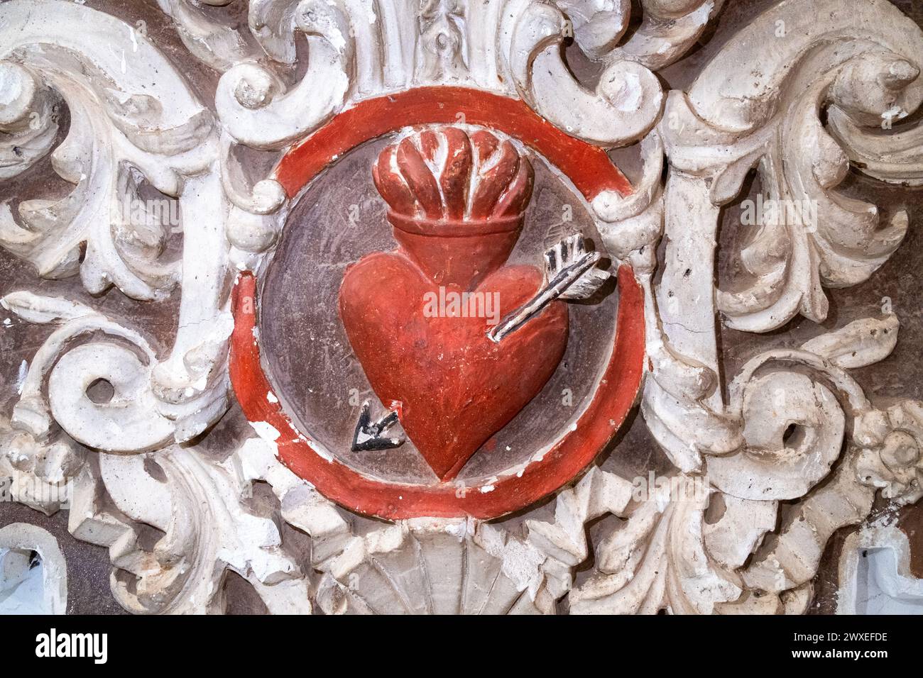 Rilievo barocco di un cuore rosso sacro trafitto da una freccia e circondato da decorazioni in gesso bianco. Dettaglio decorativo nella Chiesa di San Agustin i. Foto Stock