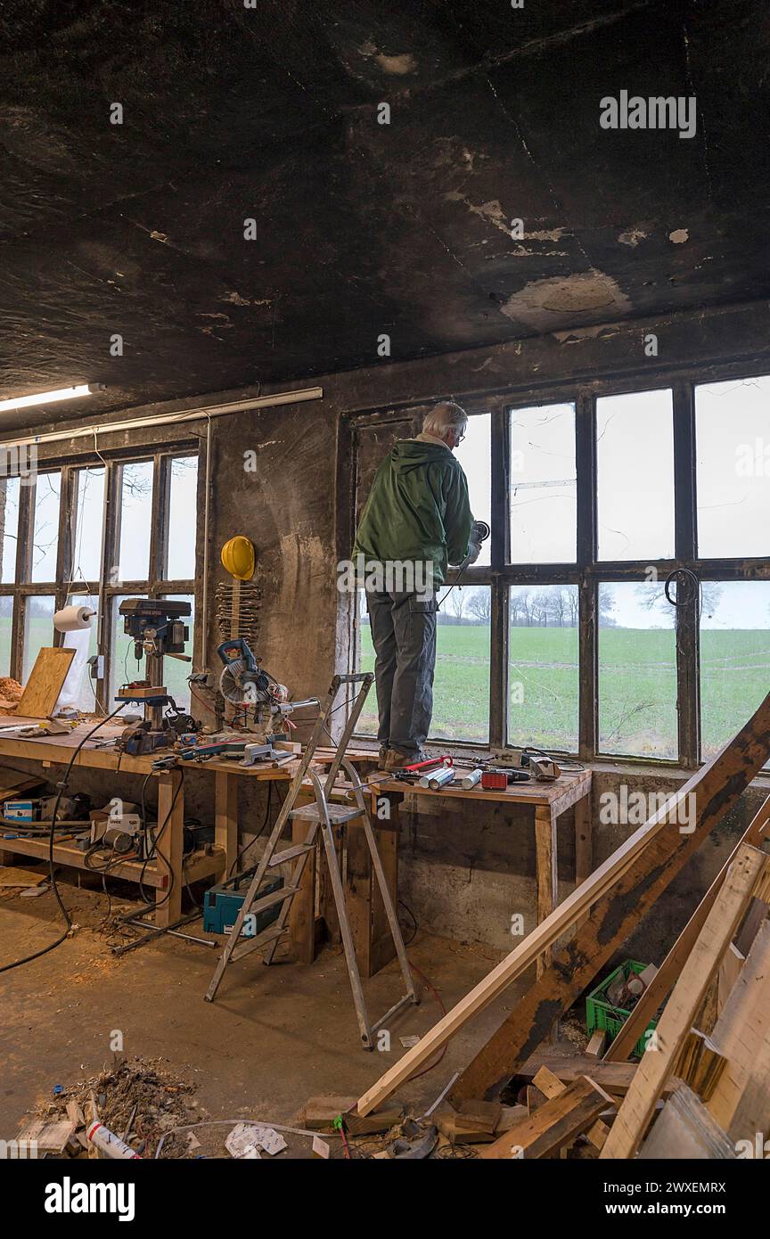 Uomo anziano in piedi su un banco di lavoro e ripara una finestra in un'officina, Meclemburgo-Vorpommern, Germania Foto Stock