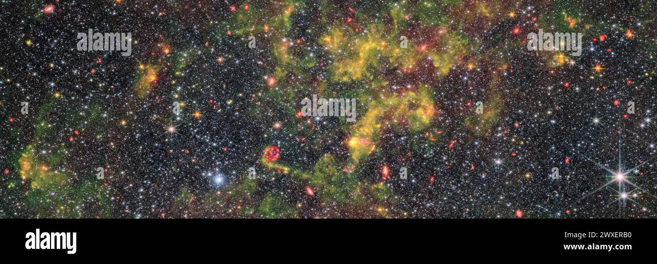 Questa immagine mostra la galassia irregolare NGC 6822, che è stata osservata dalla telecamera Near-Infrared (NIRCam) e dallo strumento Mid-Infrared (MIRA) montato sul James Webb Space Telescope. Un fitto campo di stelle con nuvole di gas e polvere che si spargono su di esso. Le nuvole sono frammentarie e voluminose, dense e luminose che oscurano il centro dell'immagine. Galassie luminose con varie forme e dimensioni brillano attraverso il gas e le stelle. Alcune delle immagini stellari sono un po' più grandi delle altre, con picchi di diffrazione visibili; due stelle in primo piano sono luminose nell'angolo inferiore destro. CREDITI: NASA/ESA/CSA Foto Stock