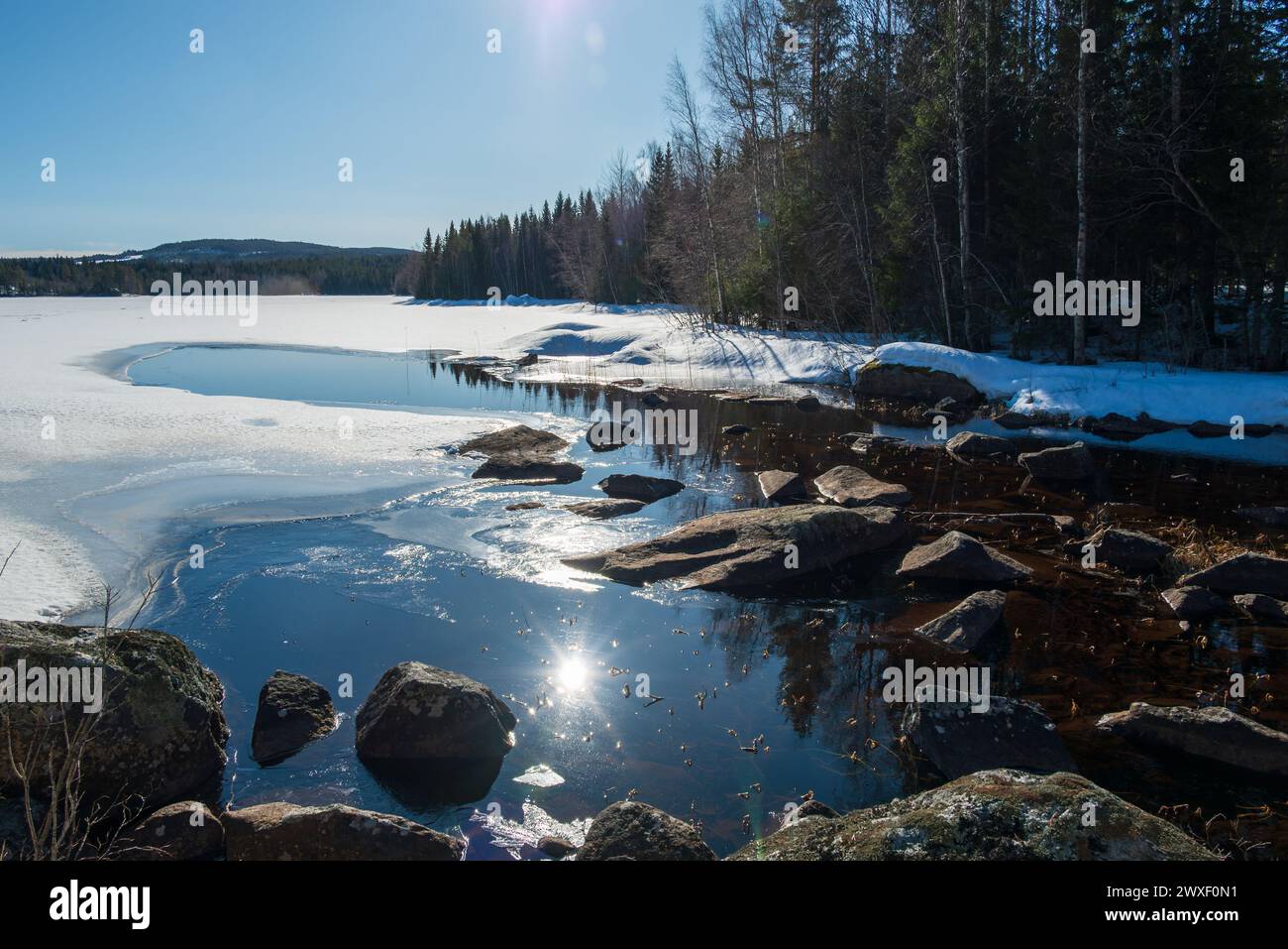 Il sole primaverile si riflette nelle acque calme di un lago che ha una piccola superficie libera dal ghiaccio vicino all'insenatura. Foto dalla vasternorrland Svezia. Foto Stock