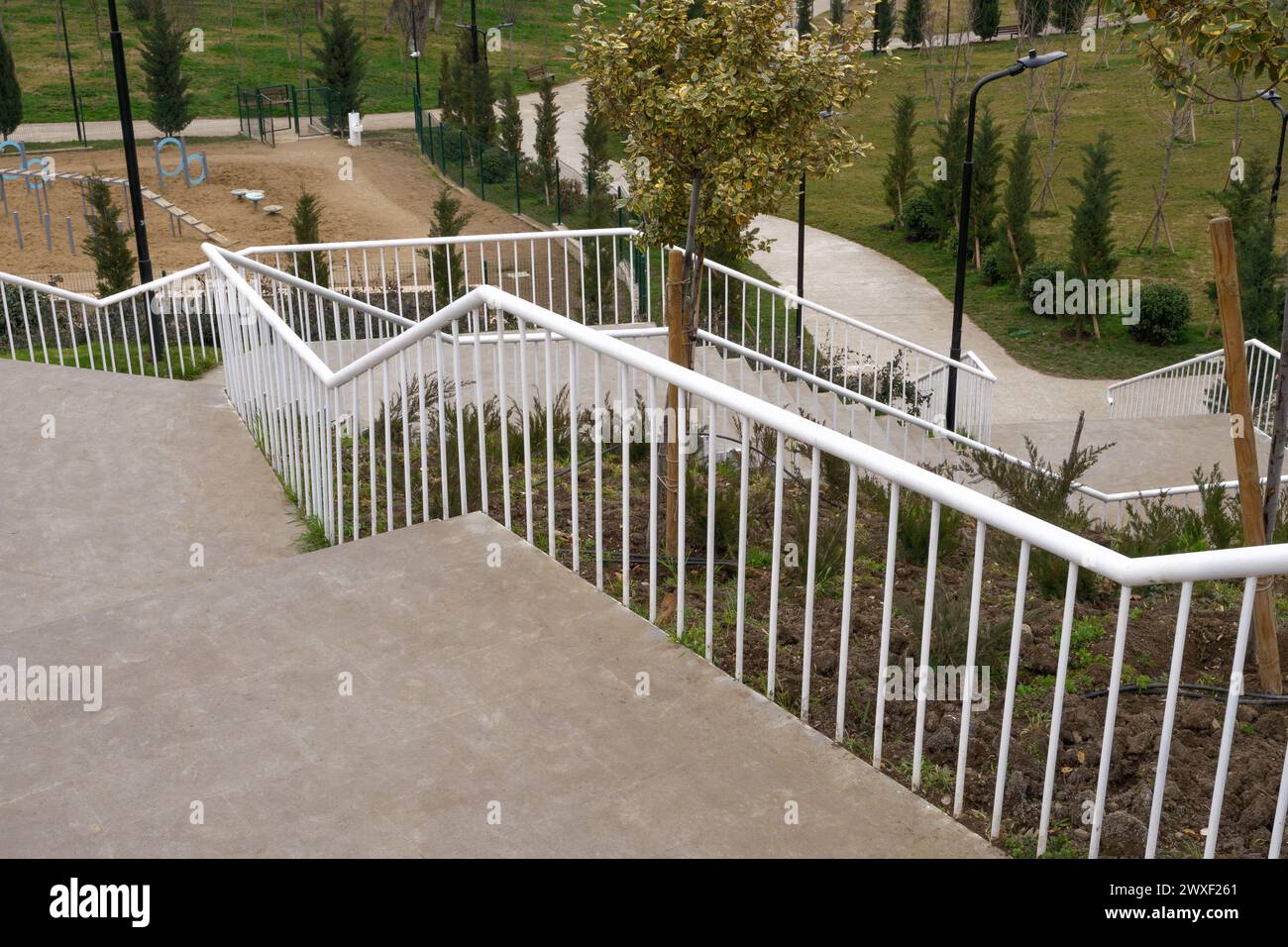 Una lunga scalinata curva con ringhiere in metallo bianco scende in una verdeggiante area del parco. Foto Stock