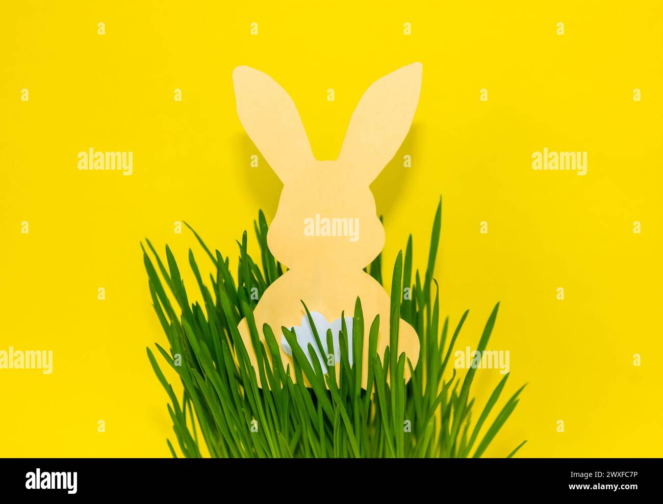 Coniglio tagliato in carta nell'erba su sfondo giallo. Per il giorno di Pasqua, invito, biglietto d'auguri, poster e sfondo. Foto Stock