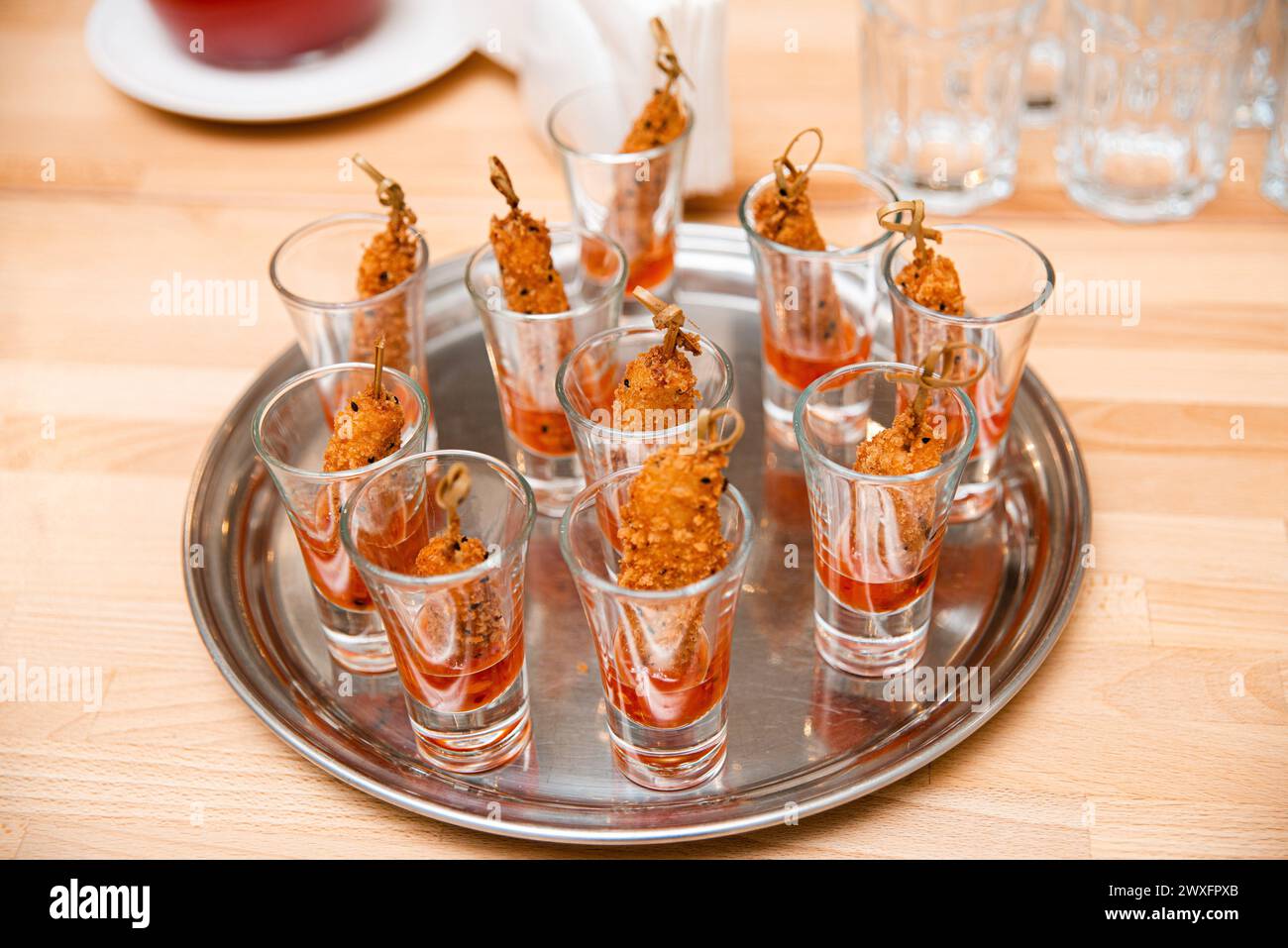 Bicchieri da shot riempiti con salsa dolce e piccante e conditi con gamberi fritti croccanti, presentati su un vassoio d'argento per un elegante evento di catering. Foto Stock