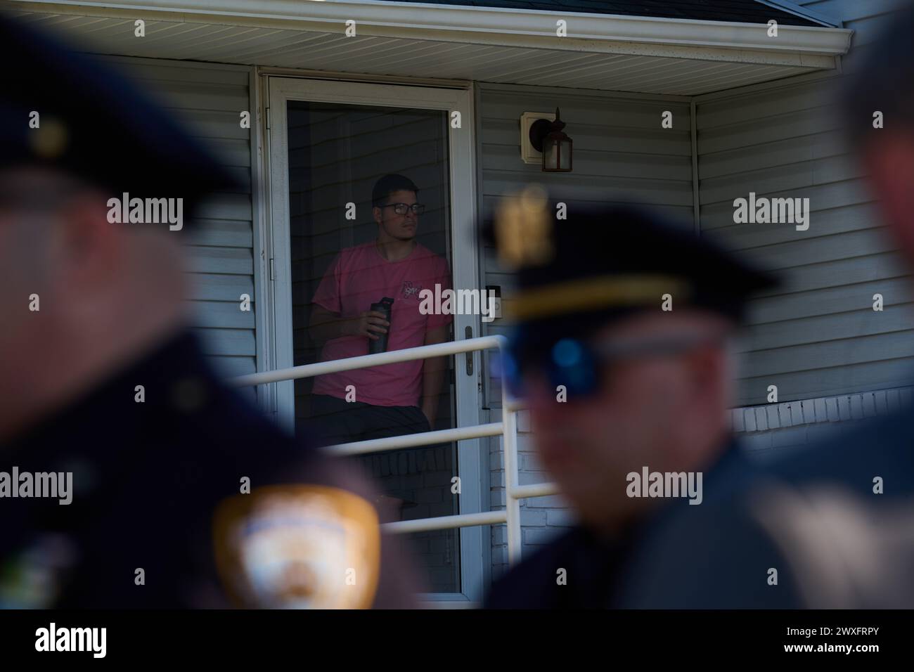 New York, New York, Stati Uniti. 30 marzo 2024. Un giovane uomo esce dalla sua porta d'ingresso mentre i membri della polizia di New York passano davanti alla sua strada di fronte a St Rose o f Lima Massapequa Church, dove migliaia di membri del NYPD e il personale delle forze dell'ordine provenienti da tutto il paese si riuniscono per il funerale dell'ufficiale 31enne Jonathan Diller, che è stato colpito e ucciso durante il servizio il 25 marzo durante una fermata del traffico nel Queens. (Credit Image: © Edna Leshowitz/ZUMA Press Wire) SOLO PER USO EDITORIALE! Non per USO commerciale! Crediti: ZUMA Press, Inc./Alamy Live News Foto Stock