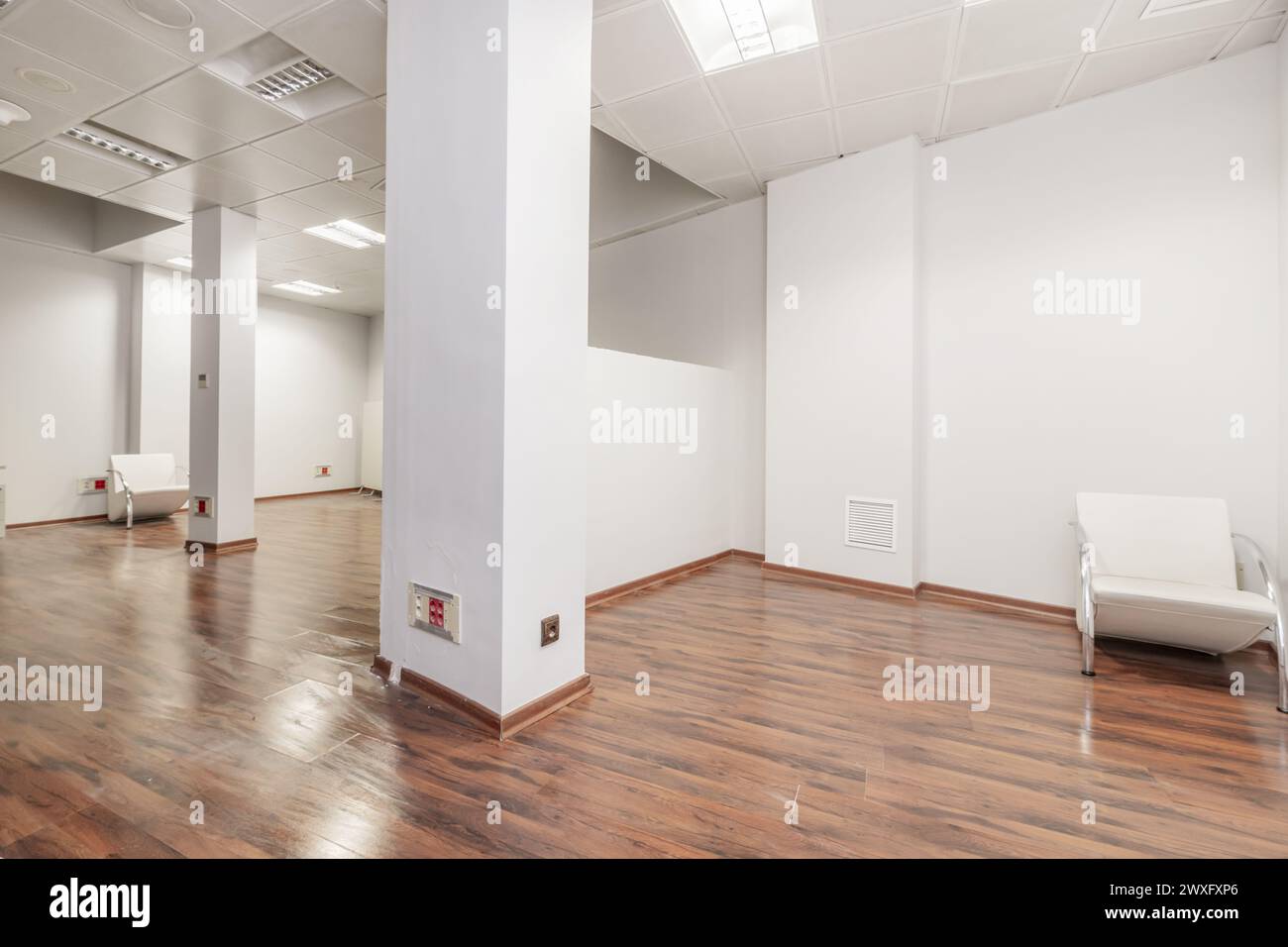 Un ufficio vuoto con diverse colonne, un muro divisorio, semplici pareti bianche e un pavimento rossastro Foto Stock