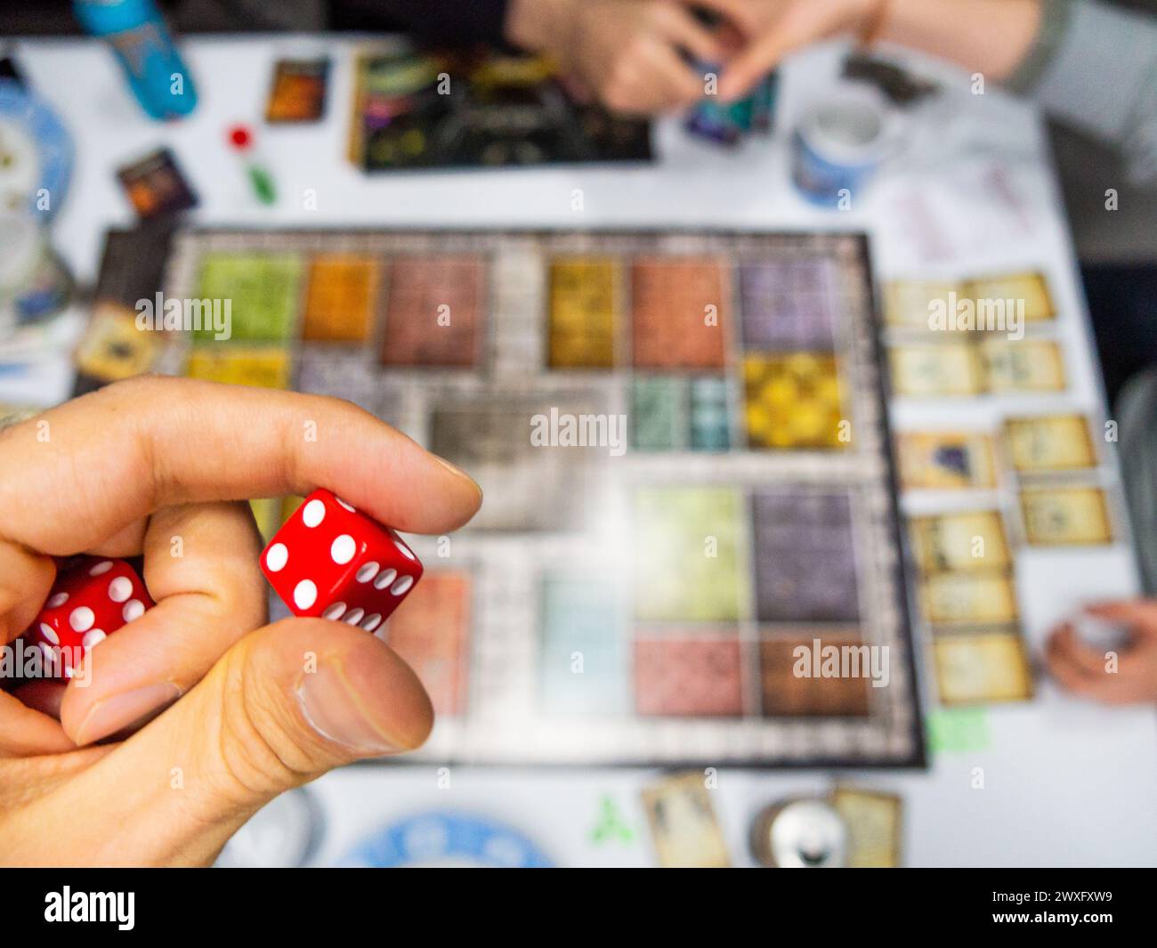 Mano con i dadi rossi a sei facce che mostrano un quattro sul tabellone dall'alto con altri giocatori reali Foto Stock