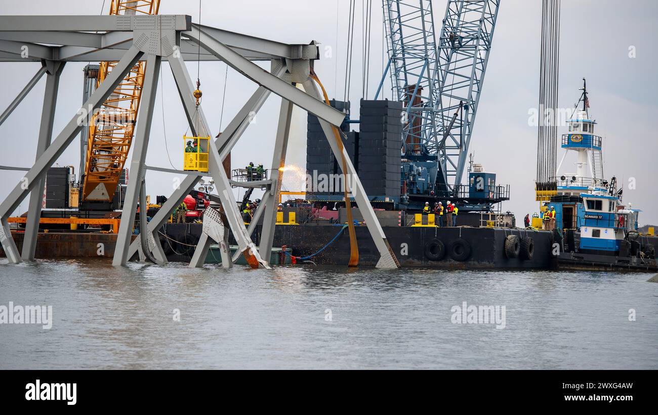 Gli equipaggi di demolizione altamente addestrati iniziarono a tagliare la parte superiore del lato nord del ponte crollato in sezioni più piccole per la rimozione sicura tramite gru nel fiume Patapsco, a Baltimora, Maryland, 30 marzo 2024. Le squadre di recupero utilizzano una torcia da taglio esotermica per separare sistematicamente sezioni del ponte in acciaio, che verrà portata in un sito di smaltimento. (Foto della Guardia Costiera degli Stati Uniti del sottufficiale di terza classe Kimberly Reaves) Foto Stock