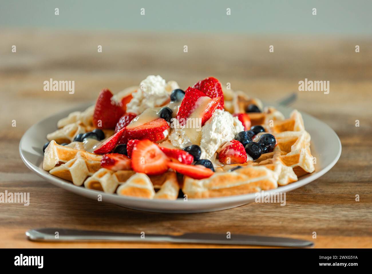 Waffle belgi dorati ricoperti di fragole, mirtilli e panna montata al momento. Una delizia appetitosa in ogni boccone per una colazione speciale. Foto Stock