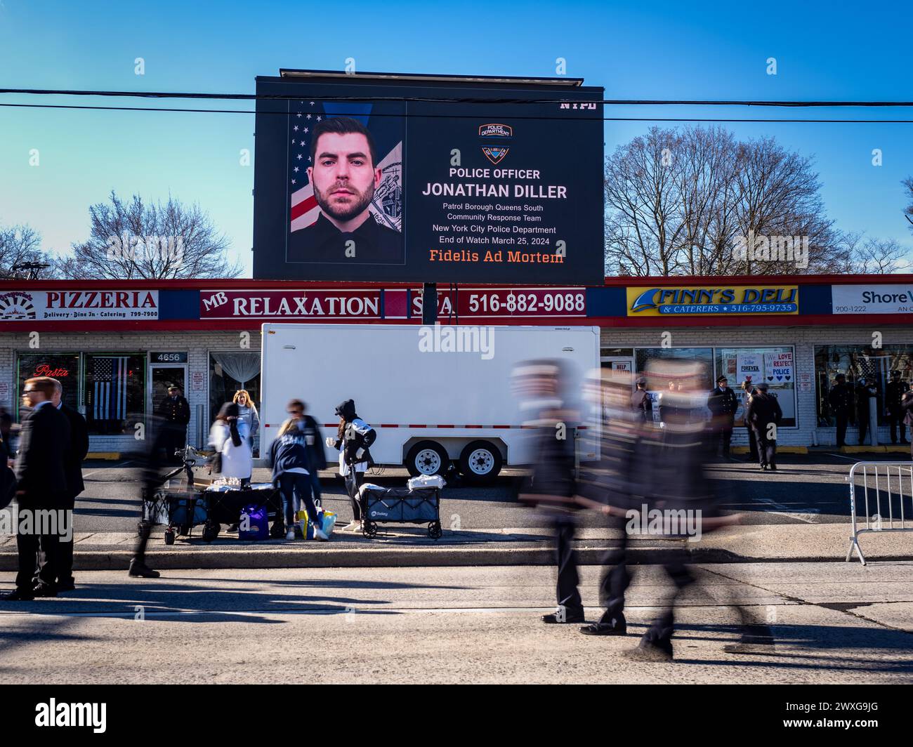 New York, Stati Uniti. 30 marzo 2024. Un segno elettronico dell'agente Jonathan Diller vicino alla chiesa. Il funerale per l'agente caduto della polizia di New York Jonathan Diller si è tenuto con centinaia di agenti di polizia allineati davanti alla St Rosa di Lima Chiesa cattolica Toman. Secondo i rapporti della polizia, l'agente Diller, di 31 anni, e il suo partner stavano facendo una fermata per un'auto parcheggiata illegalmente a far Rockaway. Durante l'incontro, un individuo nel veicolo brandiva un'arma da fuoco e la puntava agli ufficiali, provocando uno scambio di colpi di arma da fuoco. Credito: SOPA Images Limited/Alamy Live News Foto Stock