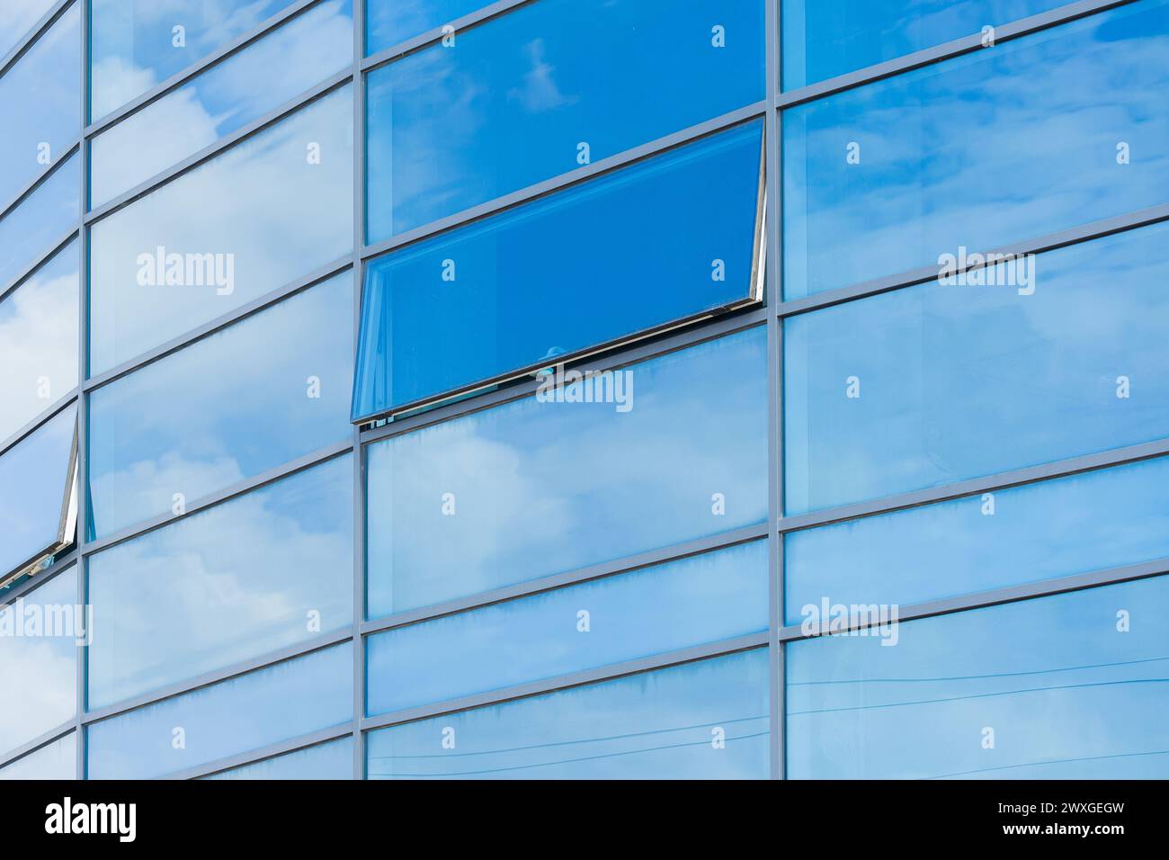 Il vetro blu riflette il cielo nuvoloso della facciata di un edificio moderno. Foto Stock