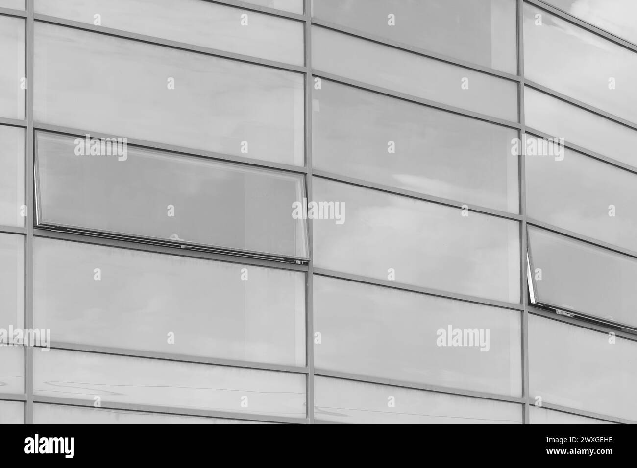 Il vetro grigio chiaro riflette il cielo nuvoloso della moderna facciata esterna dell'edificio, sfondo dalle texture degli uffici. Foto Stock