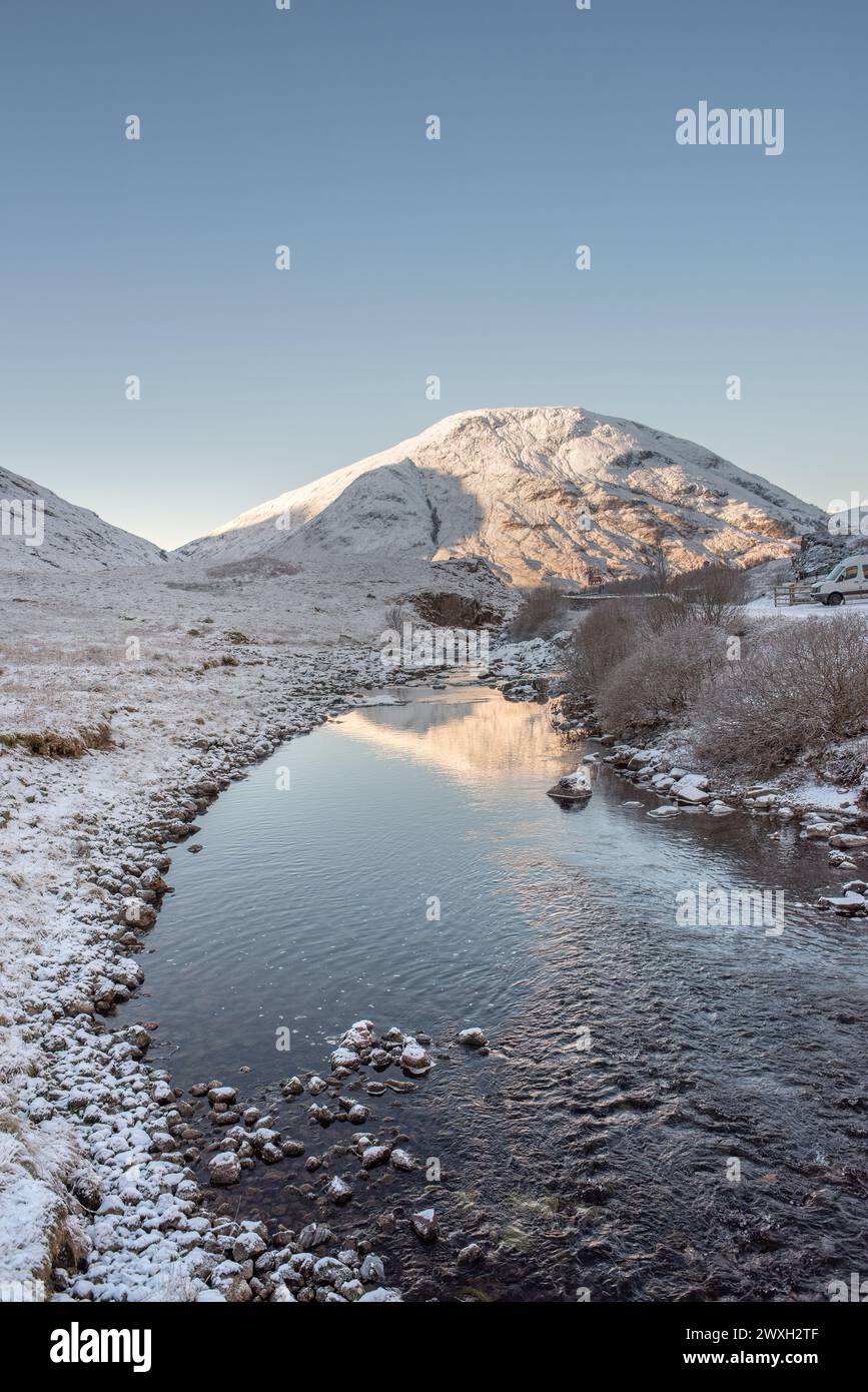 Il fiume Coe a Glencoe raggiunge le montagne innevate sotto un cielo azzurro. Highlands scozzesi, Regno Unito Foto Stock