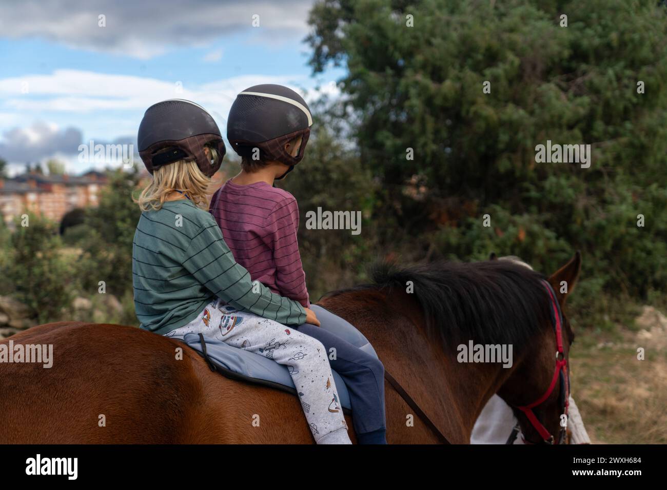 Due bambini che cavalcano insieme a cavallo facendo una passeggiata nella natura Foto Stock