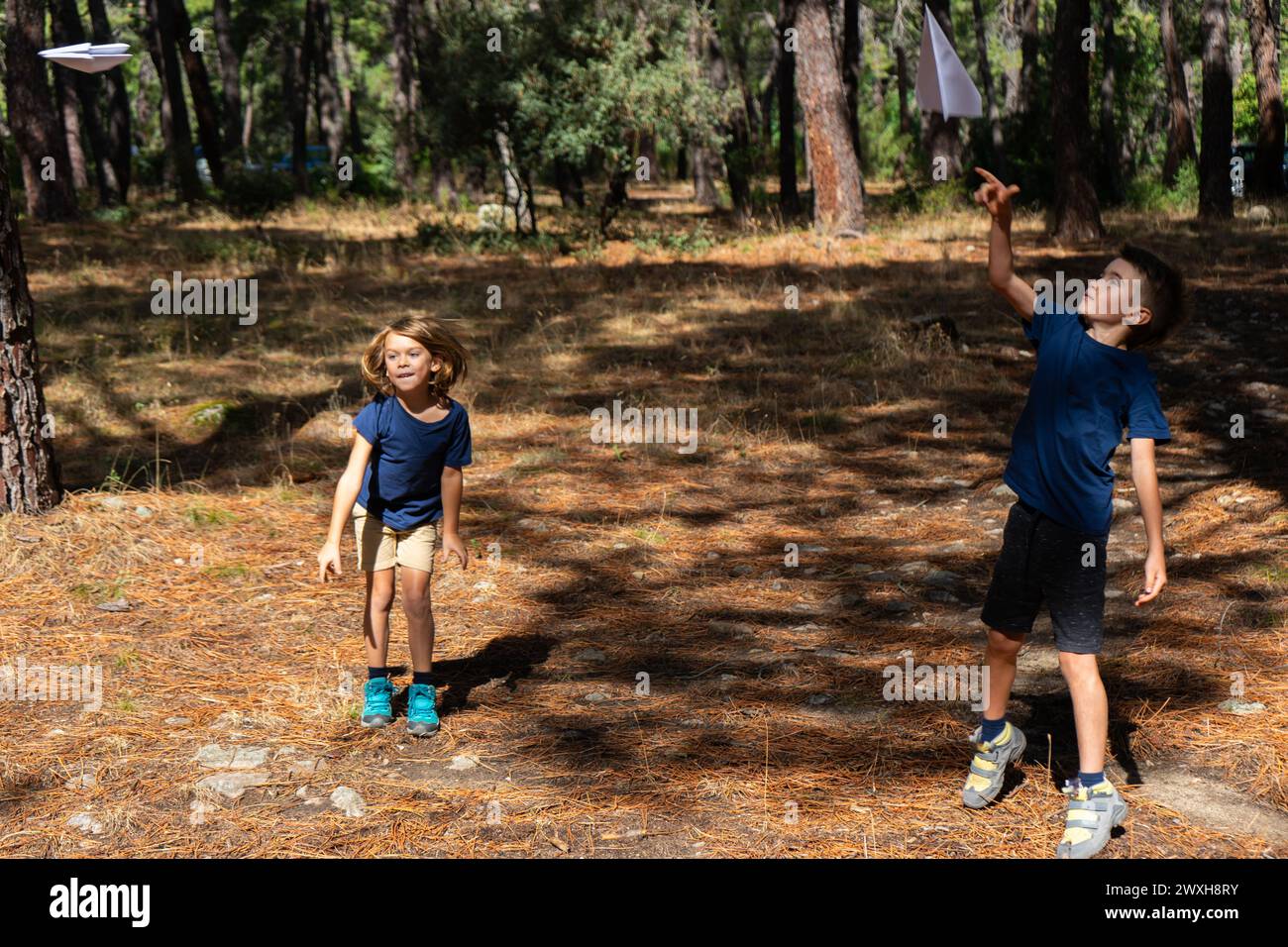 Due bambini che giocano con aerei di carta nella foresta Foto Stock