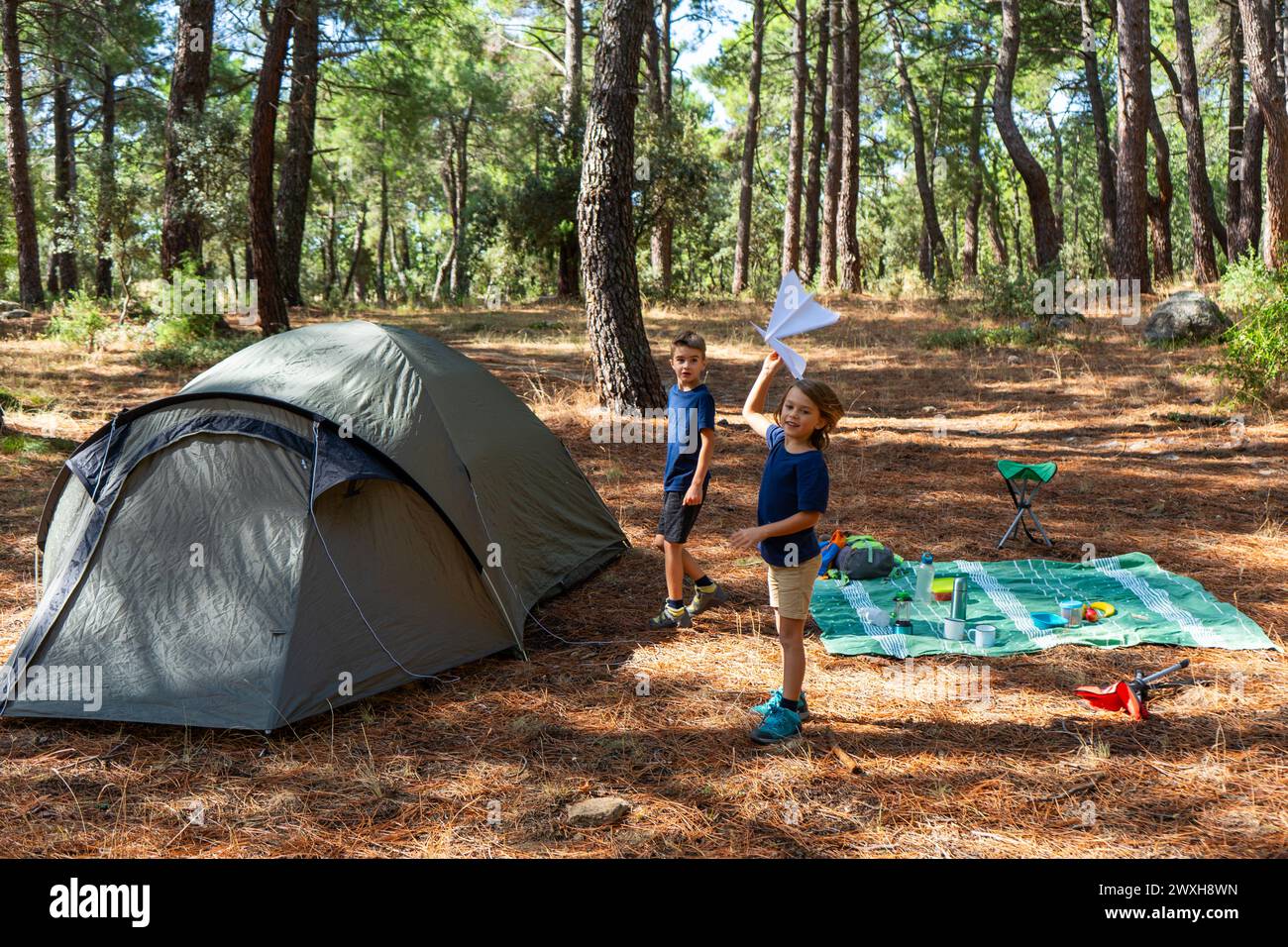 Due bambini che giocano con gli aeroplani di carta in campeggio in una foresta Foto Stock