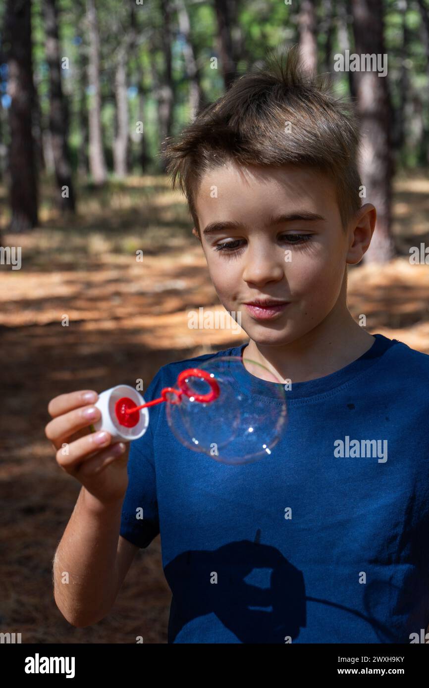 Ragazzo fiero di guardare una bolla di sapone nel bosco Foto Stock