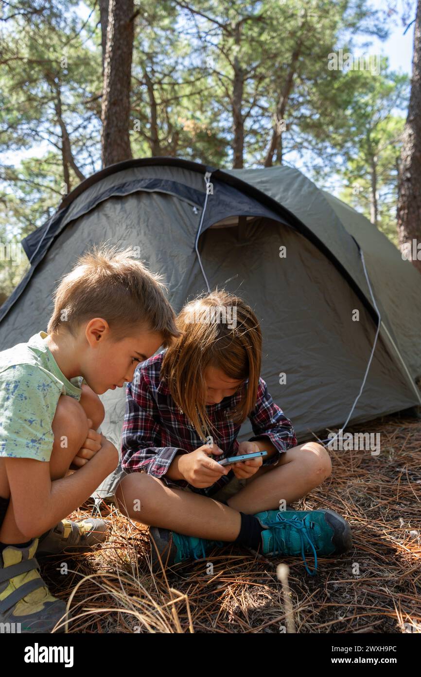 Bambini nella foresta con una tenda che guarda lo schermo mobile Foto Stock