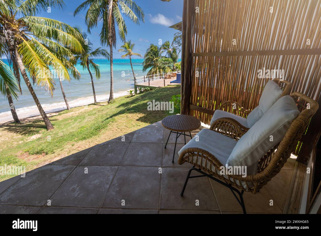 Tema vacanza caraibico. Terrazza ombreggiata con sedia e tavolo sullo sfondo blu della spiaggia Foto Stock