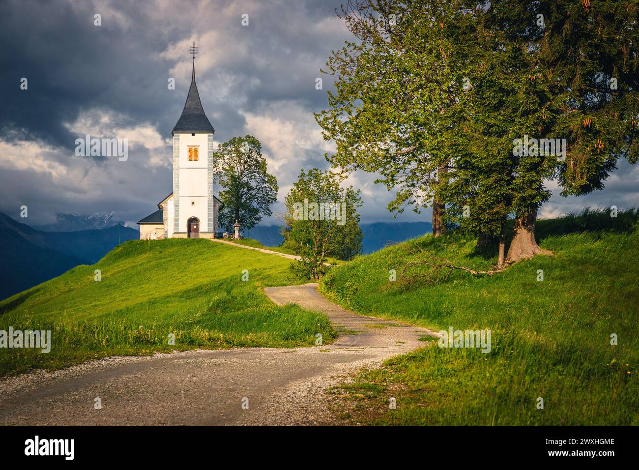 Strada rurale curva e famosa chiesa alpina sul crinale della montagna, chiesa di San Primoz, villaggio di Jamnik, Slovenia, Europa Foto Stock