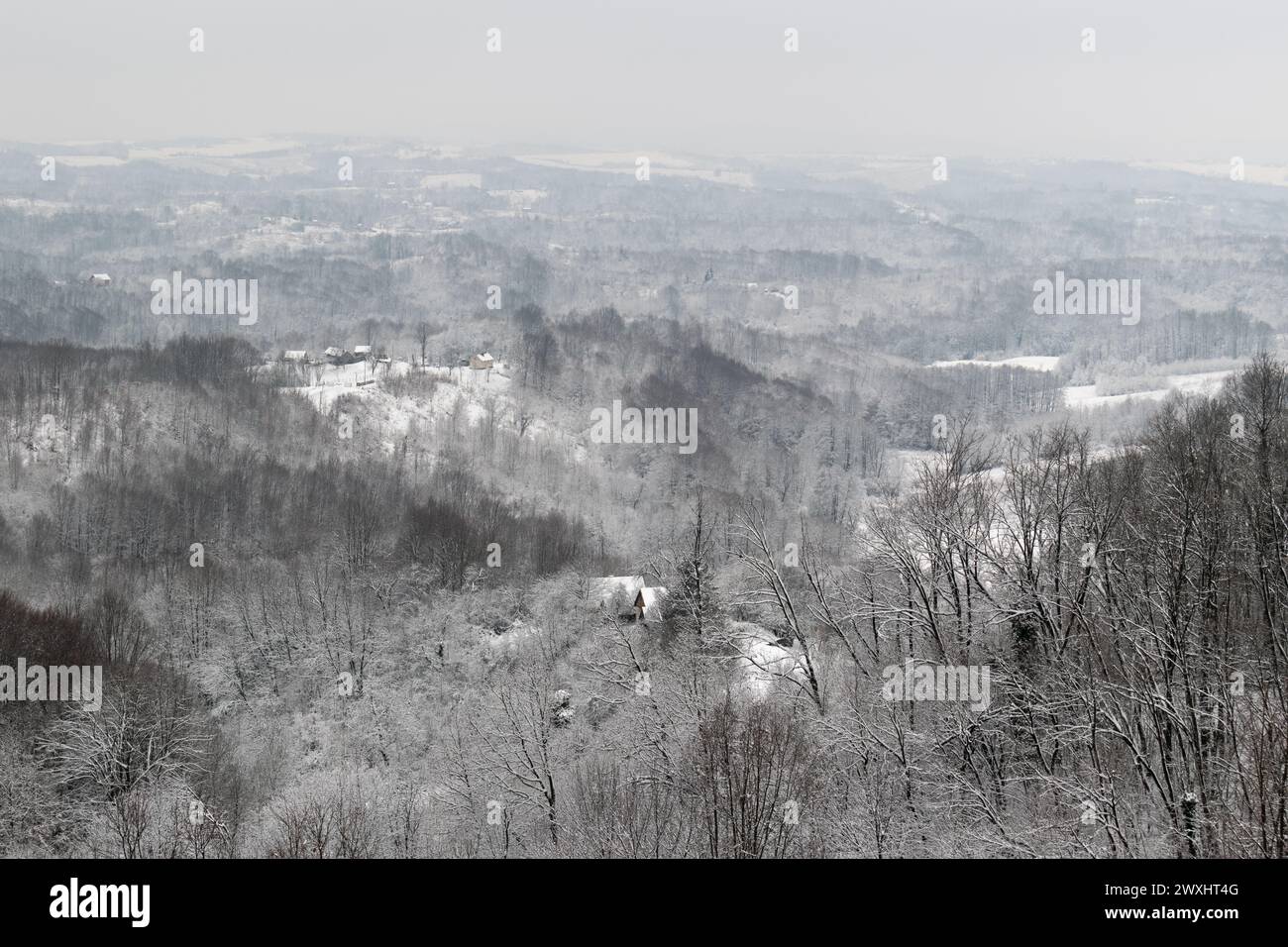 Villaggio collinare in inverno, paesaggio con foreste e case durante le fredde giornate invernali con neve e gelo Foto Stock