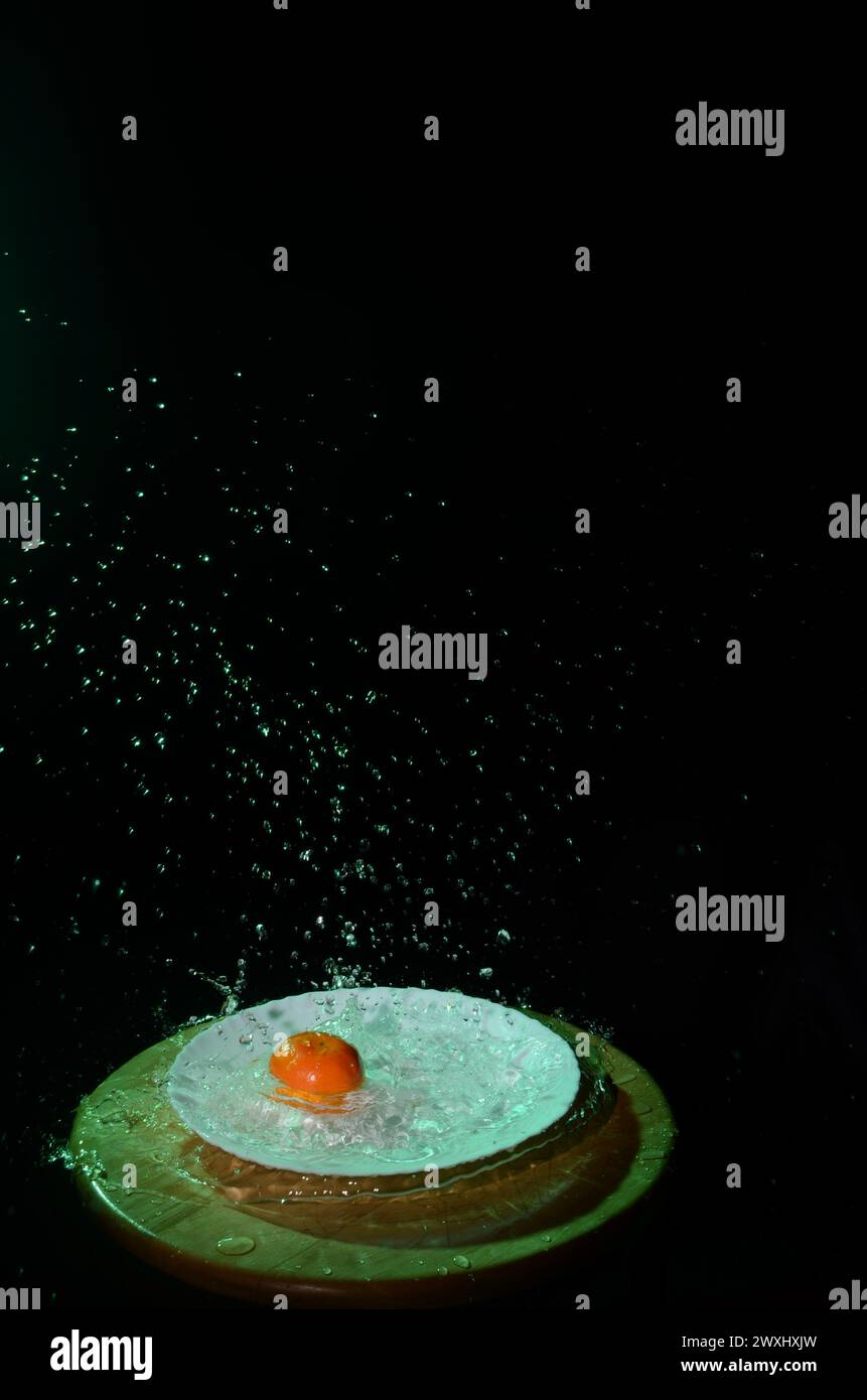 Un'arancia che cade in una ciotola d'acqua, creando uno spruzzo spettacolare su uno sfondo scuro Foto Stock