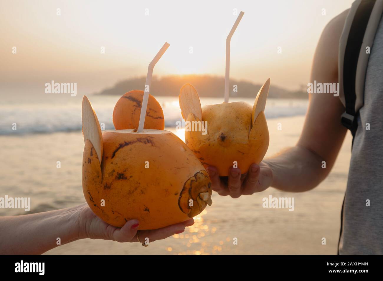 Uomo e donna bevono acqua fresca di cocco insieme su un'idilliaca spiaggia di sabbia. Sano rinfresco naturale al tramonto. Mirissa nello Sri Lanka. Foto Stock