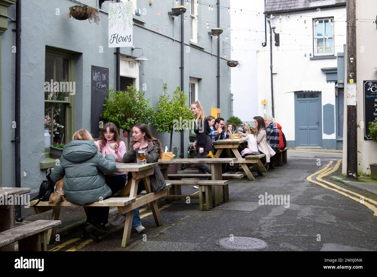 Le persone sedute ai tavoli da picnic all'aperto a pranzo mangiano e bevono al ristorante Cafe Flows on Market Street a Llandeilo, Carmarthenshire, Galles Foto Stock