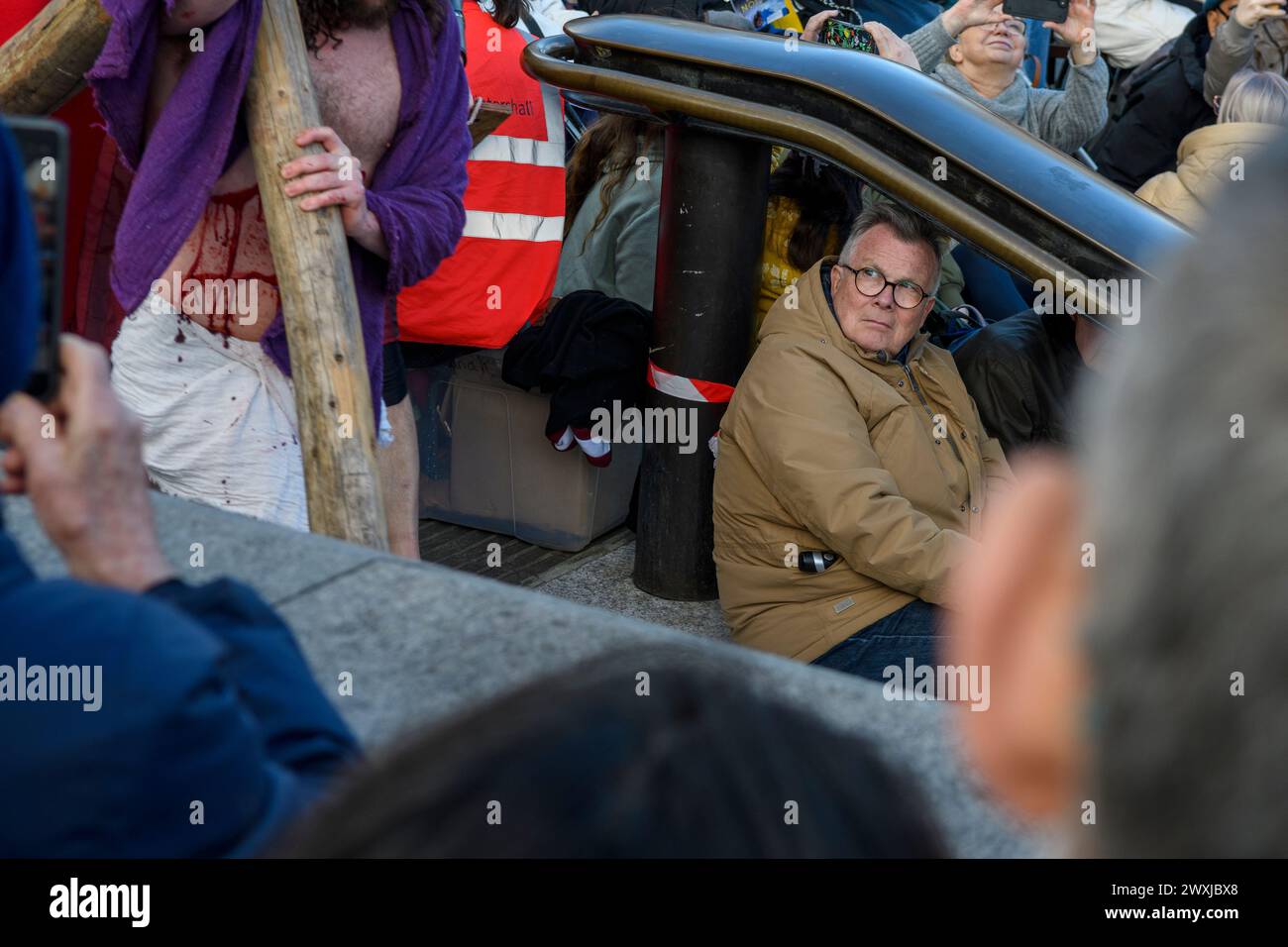 Membro del pubblico che guarda Gesù che porta una croce durante lo spettacolo Passion Play, Trafalgar Square, Londra, venerdì Santo, Pasqua, 2024 Foto Stock