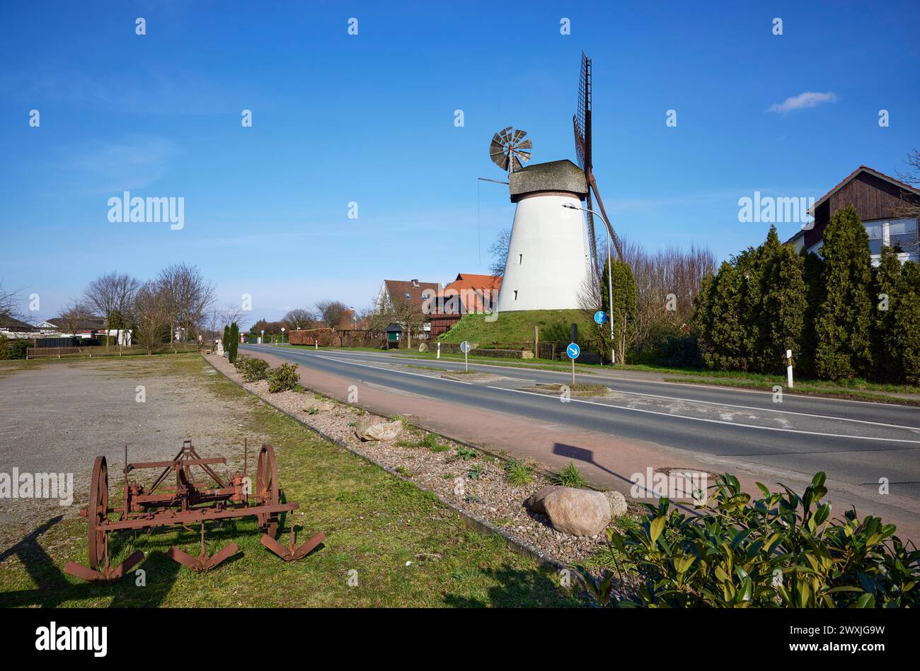 Il mulino a vento Hummelbecker Muehle sotto un cielo azzurro senza nuvole, un muro-Hollaender e un aratro storico in primo piano fa parte della Westfaelische Foto Stock
