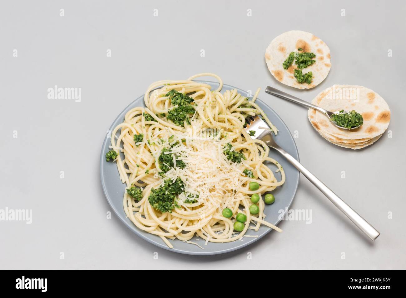 Spaghetti con pasta di broccoli e forchetta su piatto di ceramica. Focaccine con cucchiaio sul tavolo. Copia spazio. Sfondo grigio. Posizione piatta Foto Stock
