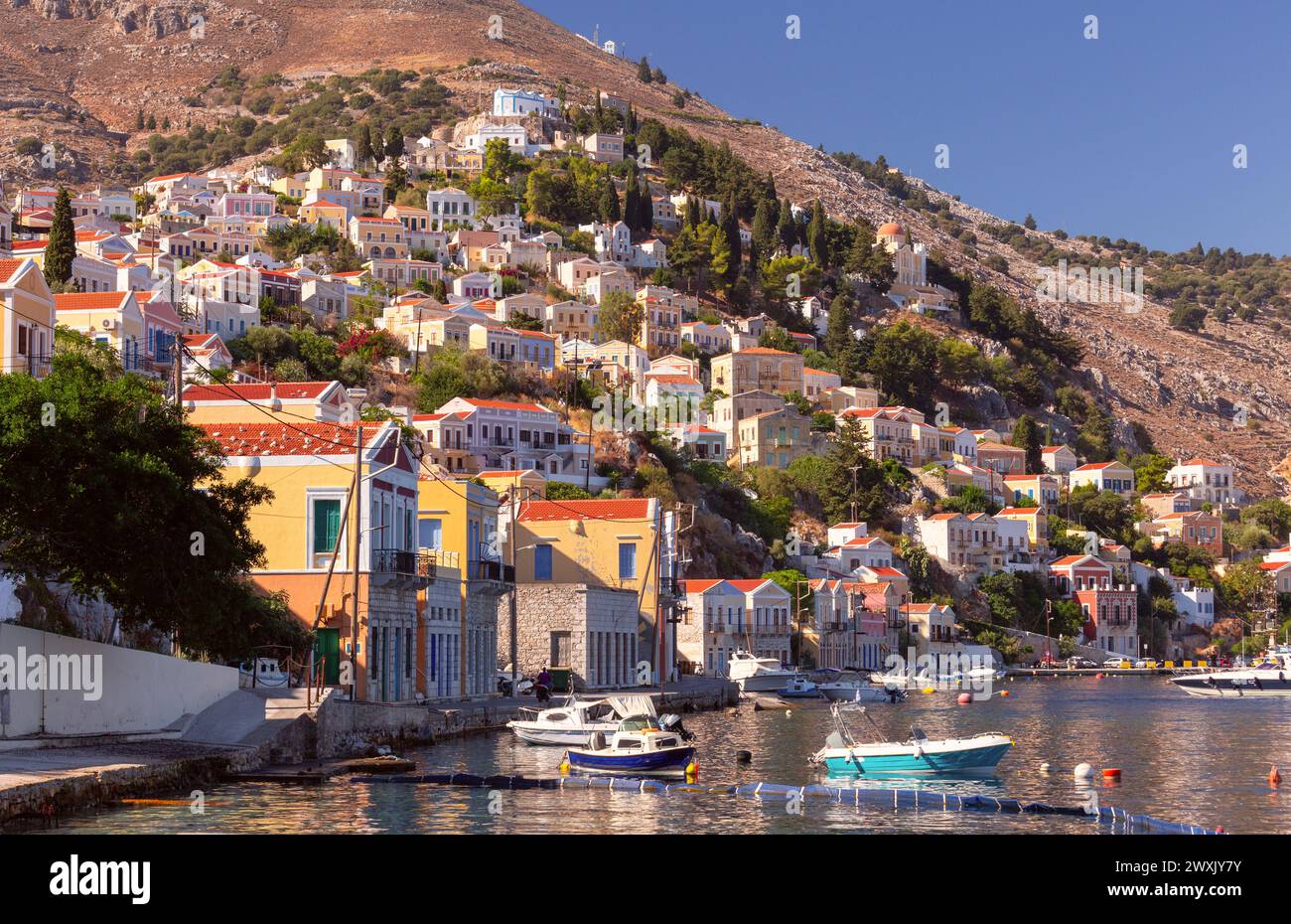 Vista delle case tradizionali colorate e delle barche da pesca nel villaggio di pescatori Symi in una giornata di sole. Grecia. Dodecaneso. Foto Stock