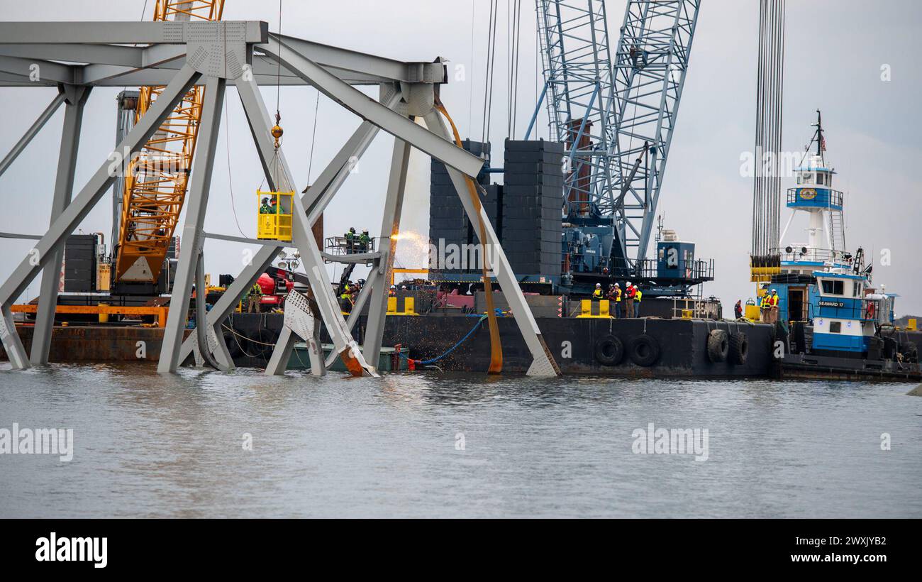 Gli equipaggi di demolizione altamente addestrati iniziarono a tagliare la parte superiore del lato nord del ponte crollato in sezioni più piccole per la rimozione sicura tramite gru nel fiume Patapsco, a Baltimora, Maryland, 30 marzo 2024. Le squadre di recupero utilizzano una torcia da taglio esotermica per separare sistematicamente sezioni del ponte in acciaio, che verrà portata in un sito di smaltimento. (Foto della Guardia Costiera degli Stati Uniti del sottufficiale di terza classe Kimberly Reaves) Foto Stock