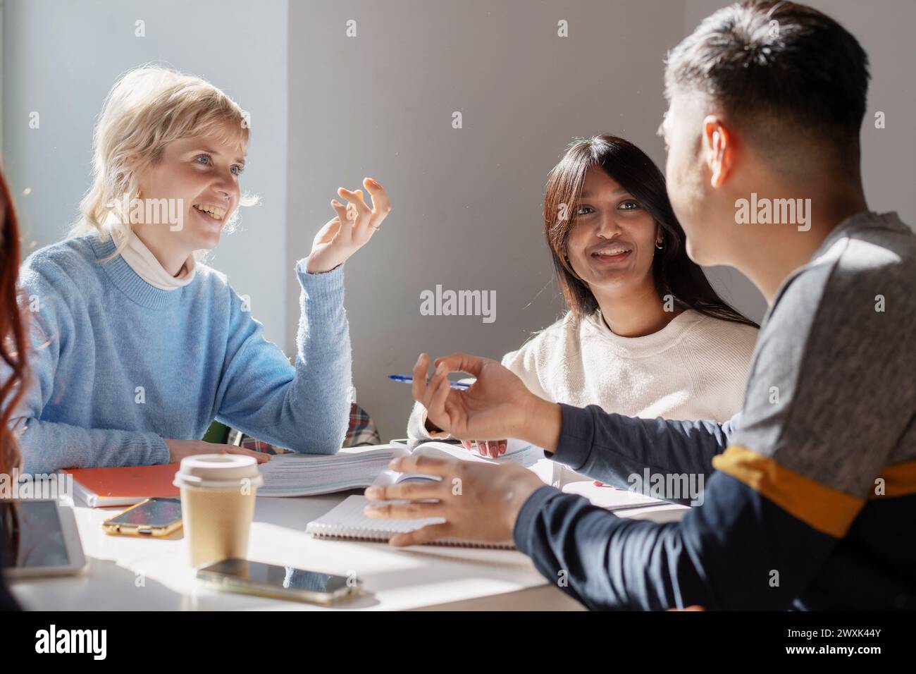 Un gruppo di studenti concentrati si impegna attivamente in discussioni accademiche, illustrando le dinamiche dell'apprendimento collaborativo in un ambiente luminoso in classe Foto Stock