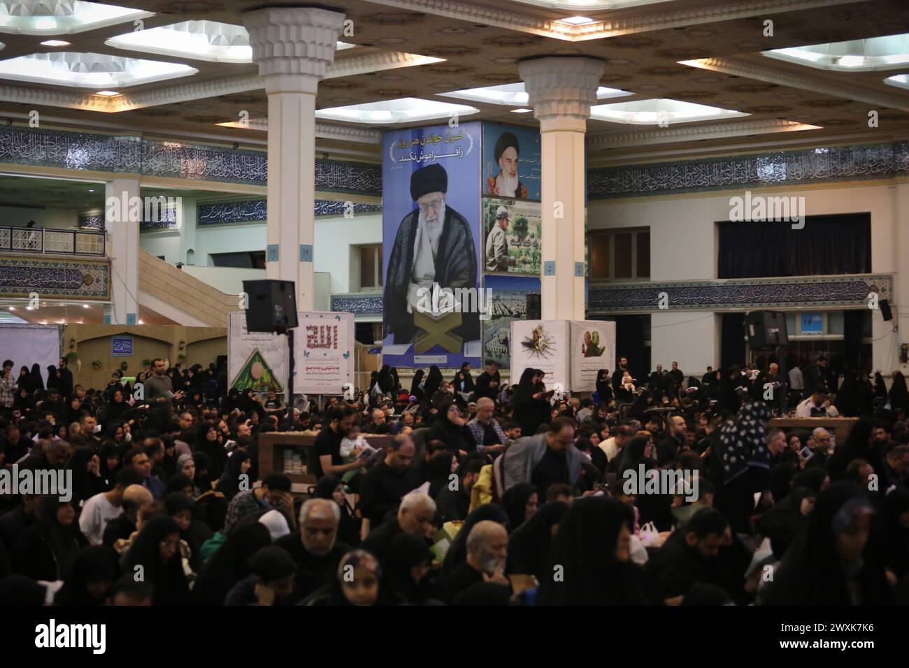 Teheran, Iran. Teheran, Iran. 1 aprile 2024. I fedeli iraniani si siedono sotto un ritratto gigante del leader iraniano Ayatollah Ali Khamenei durante la notte del potere come parte di una commemorazione che segna l'anniversario del martirio dell'Imam Ali nel mese del santo digiuno del Ramadan presso la moschea Grand Mosalla di Teheran. Il mese santo dei musulmani del Ramadan è il nono mese del calendario islamico e si ritiene che la rivelazione del primo versetto nel Corano sia avvenuta durante le sue ultime 10 notti. Crediti: ZUMA Press, Inc./Alamy Live News Foto Stock