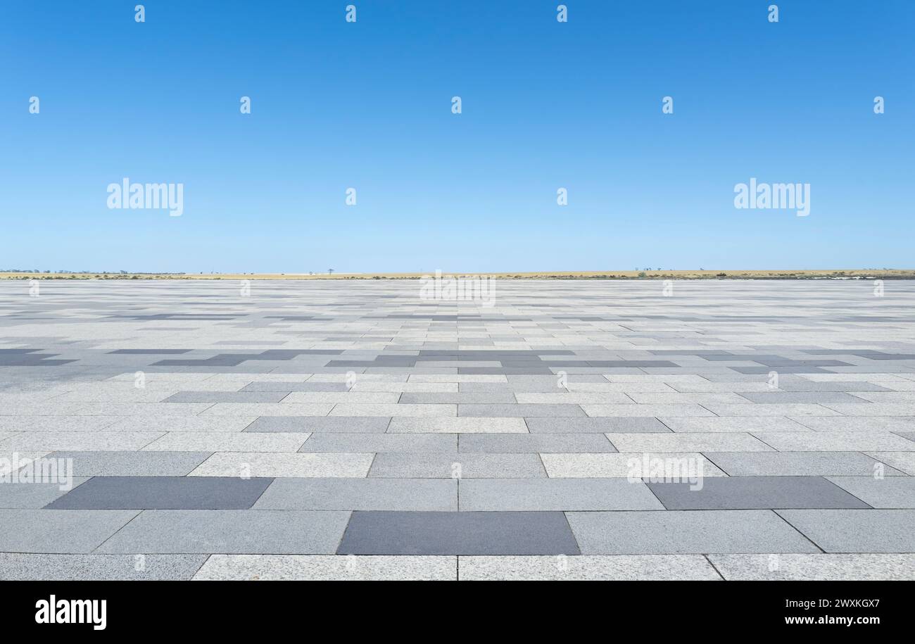 Un pavimento vuoto in cemento si estende verso l'esterno con un cielo azzurro limpido sullo sfondo. La semplicità della scena mette in risalto l'ampio spazio aperto e il mini Foto Stock