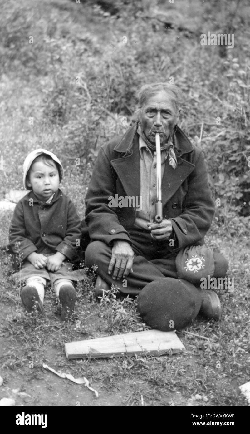 Sisseton-Wahpeton Oyate della riserva Lake Traverse, South Dakota: Anziano uomo nativo americano, John Bear, che fuma una pipa con un bambino seduto accanto a lui CA. 1937 Foto Stock