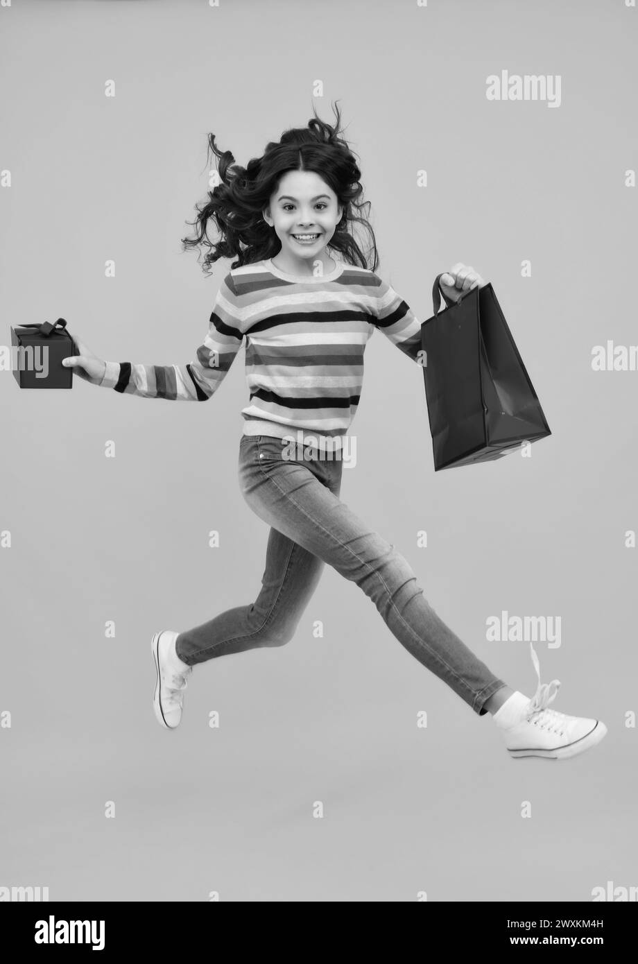 Bambino ragazza tenere borsa shopping godendo vendita isolato su sfondo giallo. Ritratto di ragazza adolescente è pronto per andare a fare shopping. Corri e salta. Foto Stock