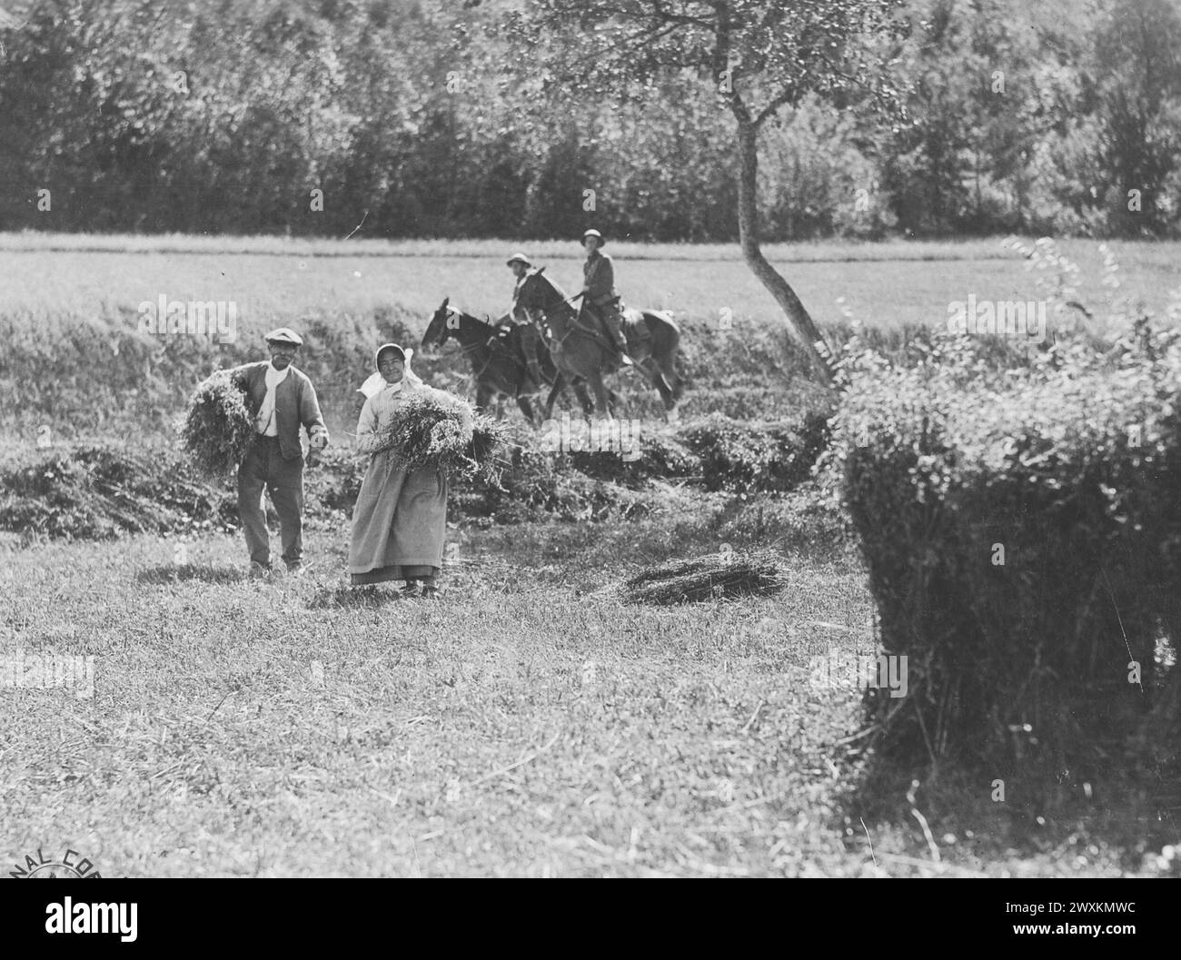 Un uomo e una donna nella loro fattoria che raccolgono con cavalieri di spedizione a cavallo delle truppe del quartier generale, la 33rd Division, possono essere visti passare sullo sfondo; Willencourt Meuse, Francia ca. 1918 Foto Stock