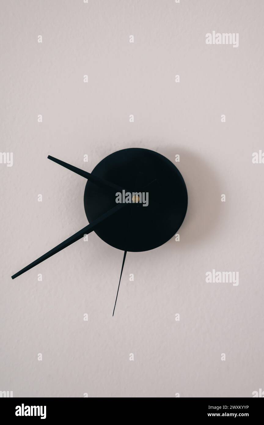 Orologio nero appeso su un muro bianco Foto Stock